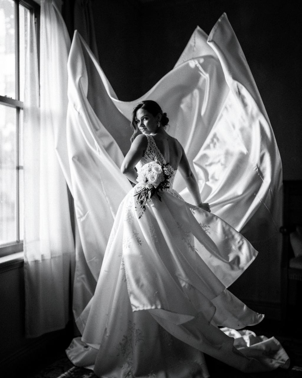 Bride turning in a flowing silk gown beside a bright window