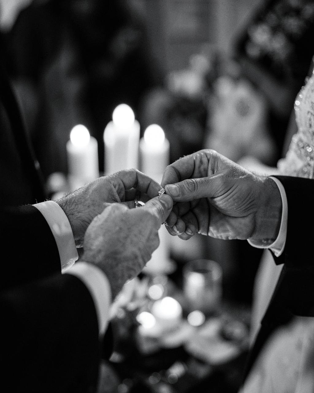 Close-up of hands exchanging a wedding ring by candlelight